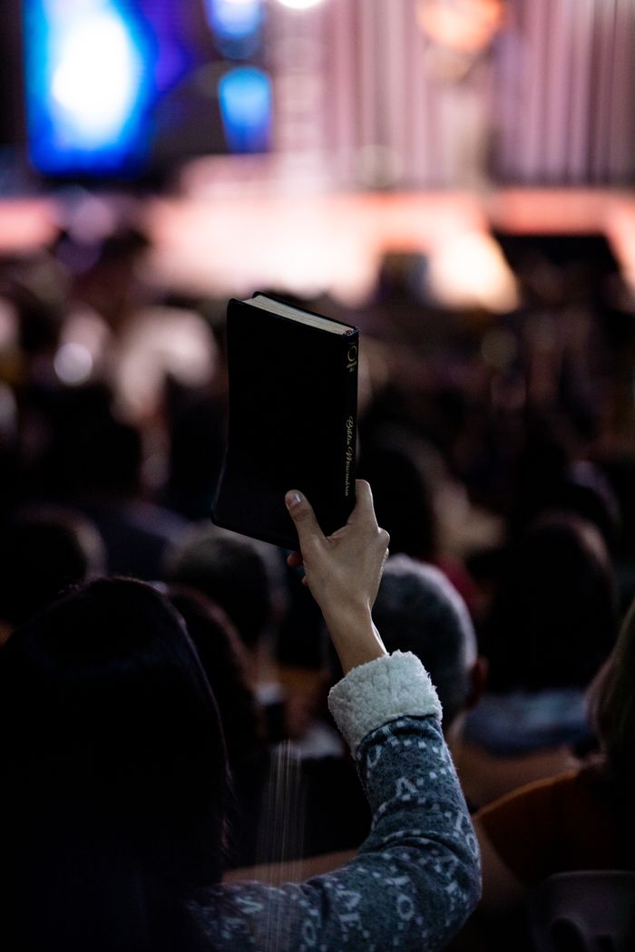 A person holds up a Bible during an indoor religious gathering, highlighting faith.